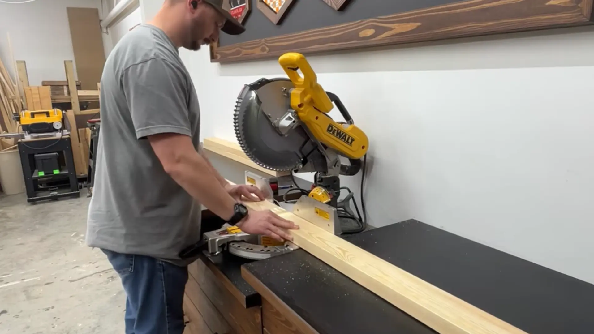 Person cutting a wooden plank using a DeWalt miter saw in a workshop.