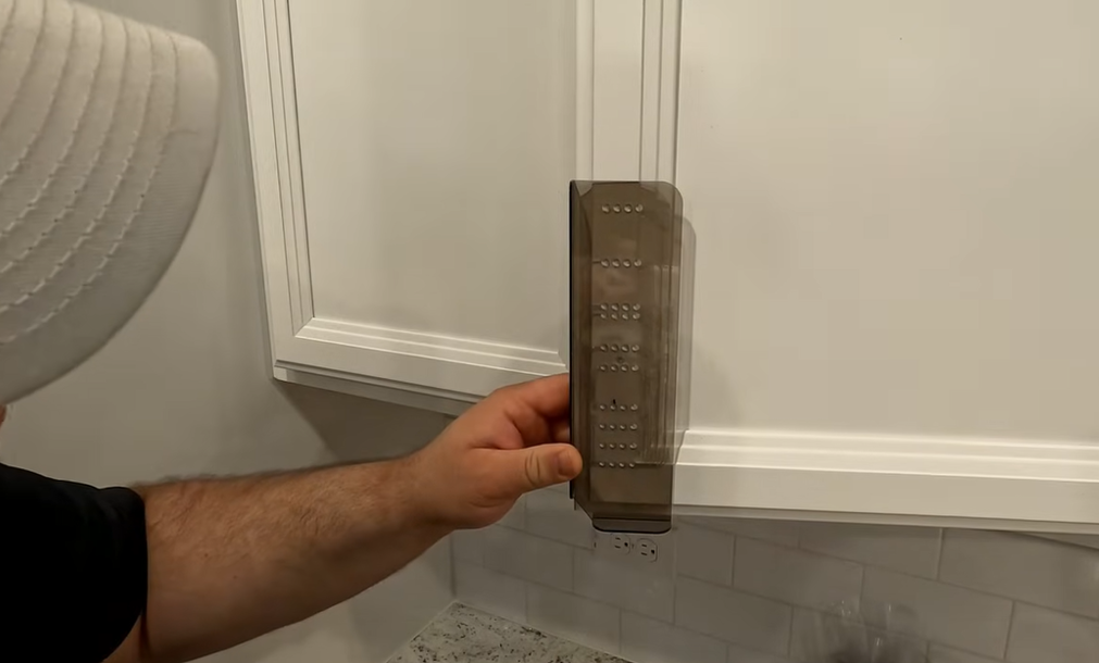 Person holding a cabinet hardware jig against a cabinet door to position drill holes for handle installation