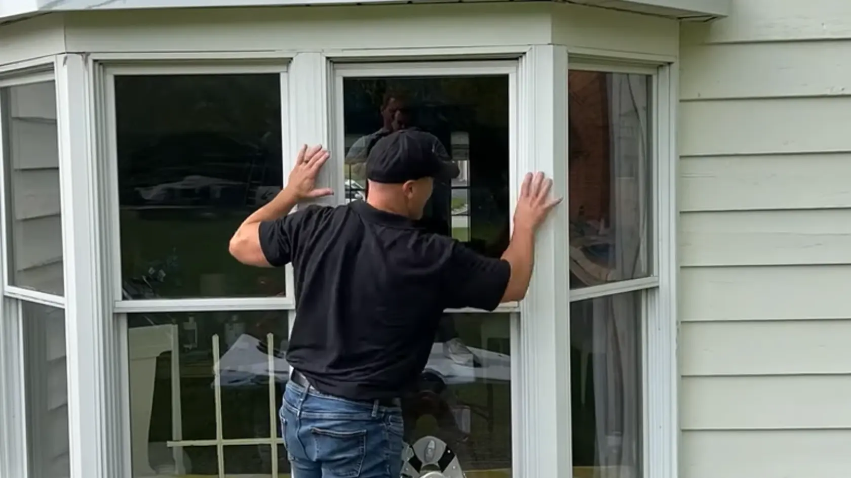 Person installing or adjusting a large replacement window panel on the exterior of a house near a ladder