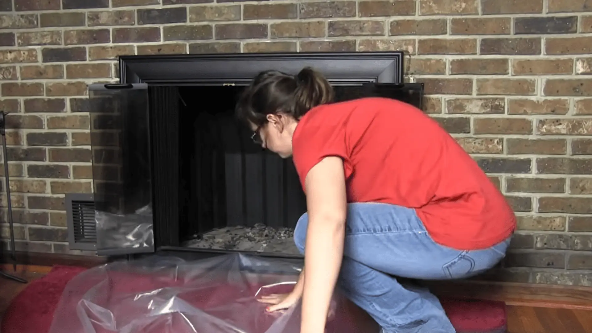 Person placing plastic drop cloth in front of fireplace to protect floor before chimney cleaning