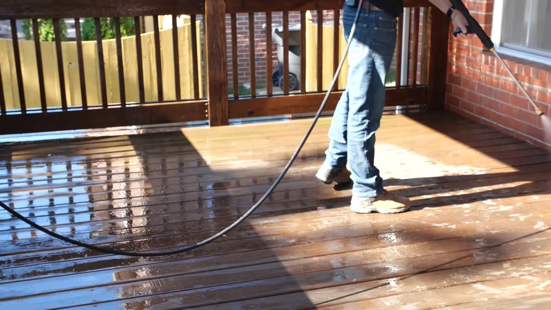 Person pressure washing a wooden deck to remove dirt and prepare it for staining