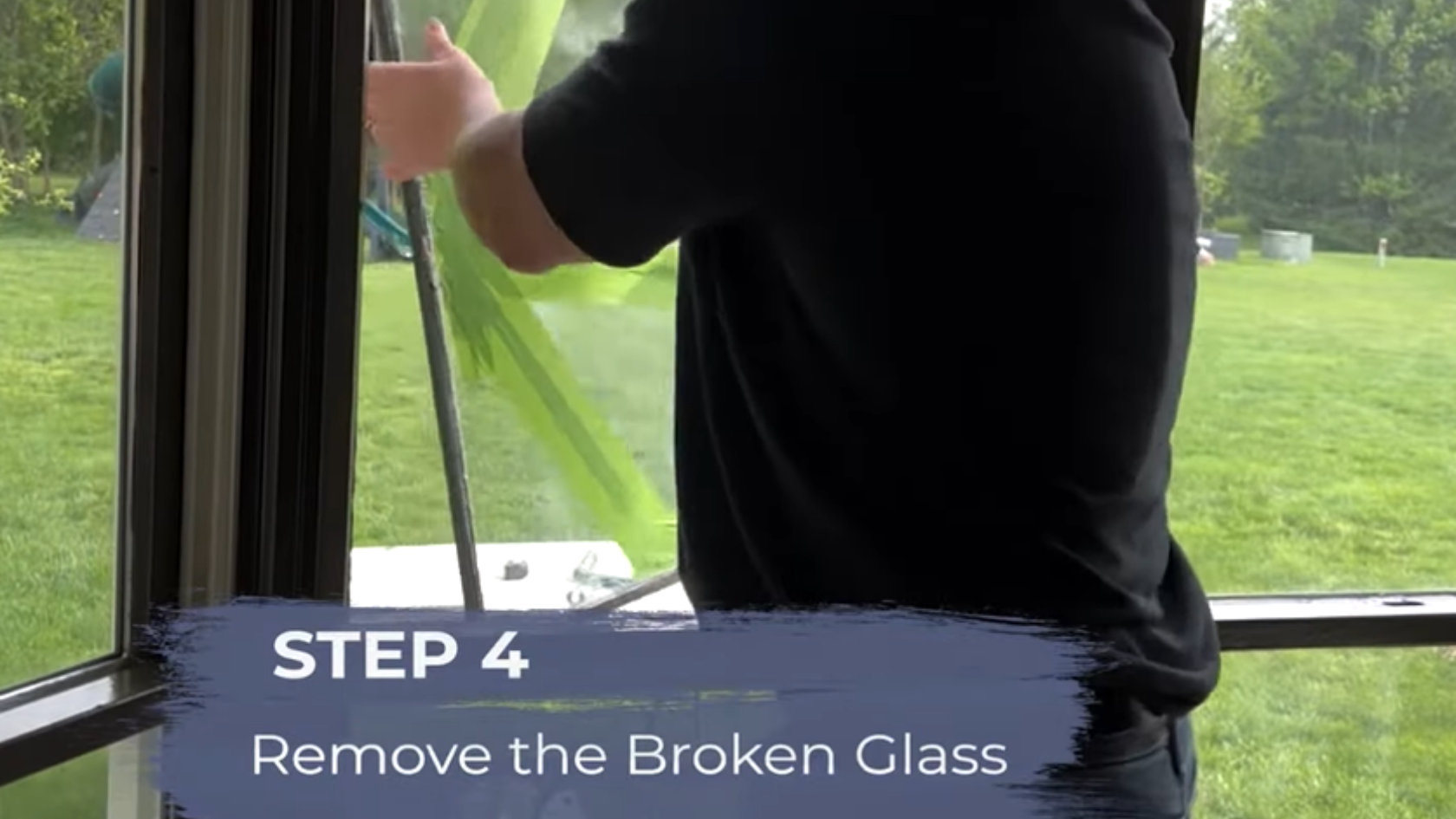 Person removing a broken window pane with green tape applied across the cracked glass and step instruction overlay