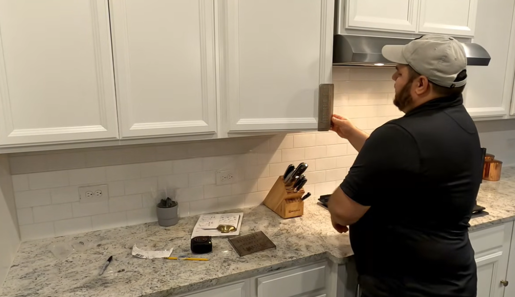 Person using a cabinet hardware jig to mark drill holes on a kitchen cabinet door before installing handles