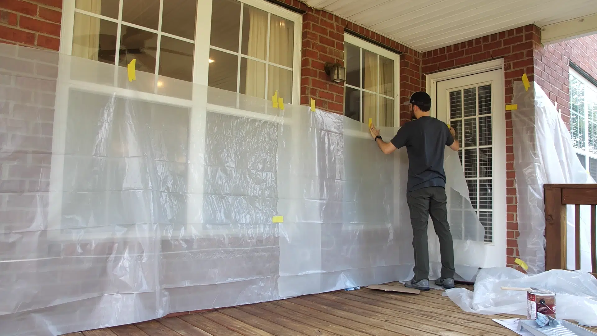Plastic sheeting taped around the perimeter of a deck, protecting nearby house siding and windows from stain overspray