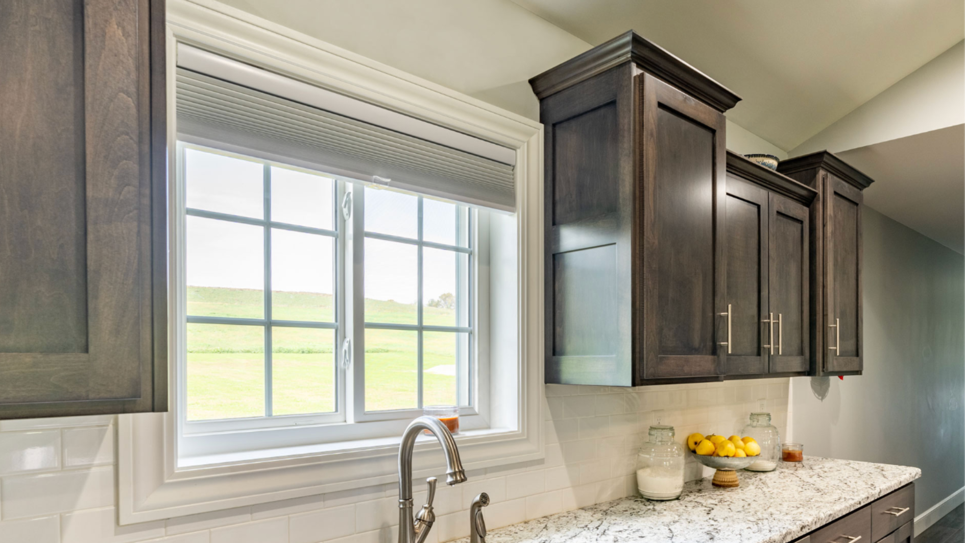 proVia casement window installed above a kitchen sink with clean white frame dark wood cabinetry granite countertop and green field view outside