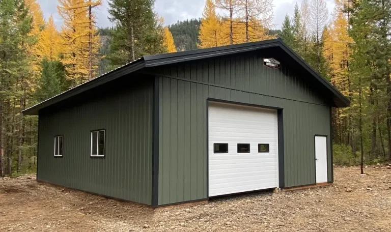 Green metal building with white garage door in a forested area featuring tall trees