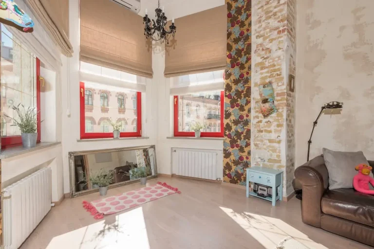 Bright living room with red-trimmed windows, floral wallpaper, and a brown leather sofa