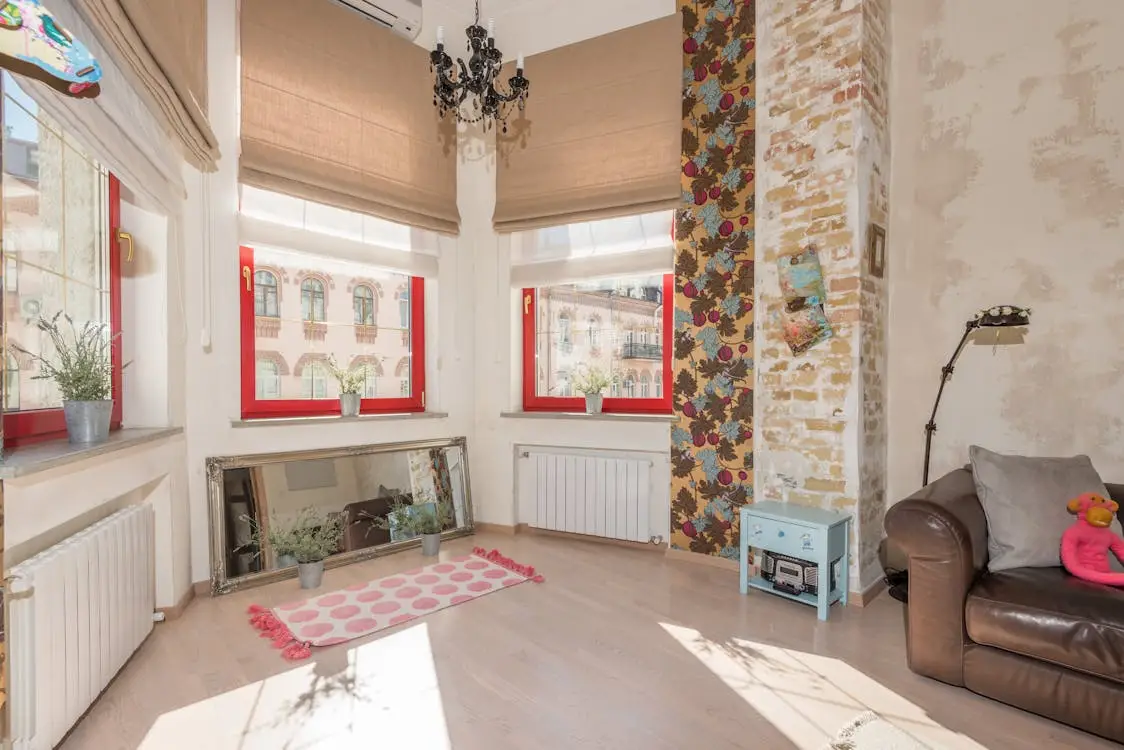 Bright living room with red-trimmed windows, floral wallpaper, and a brown leather sofa