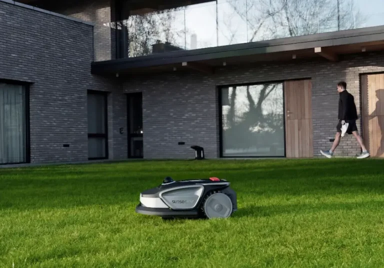 Robotic lawn mower on green grass in front of modern house with brick facade