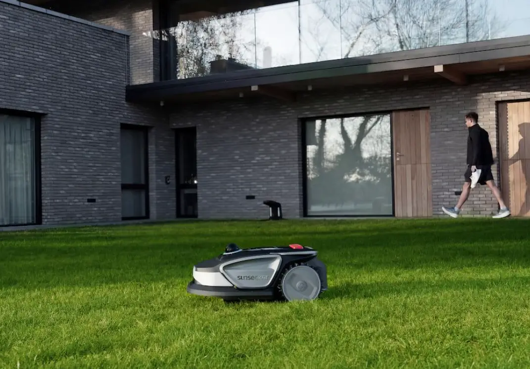 Robotic lawn mower on green grass in front of modern house with brick facade
