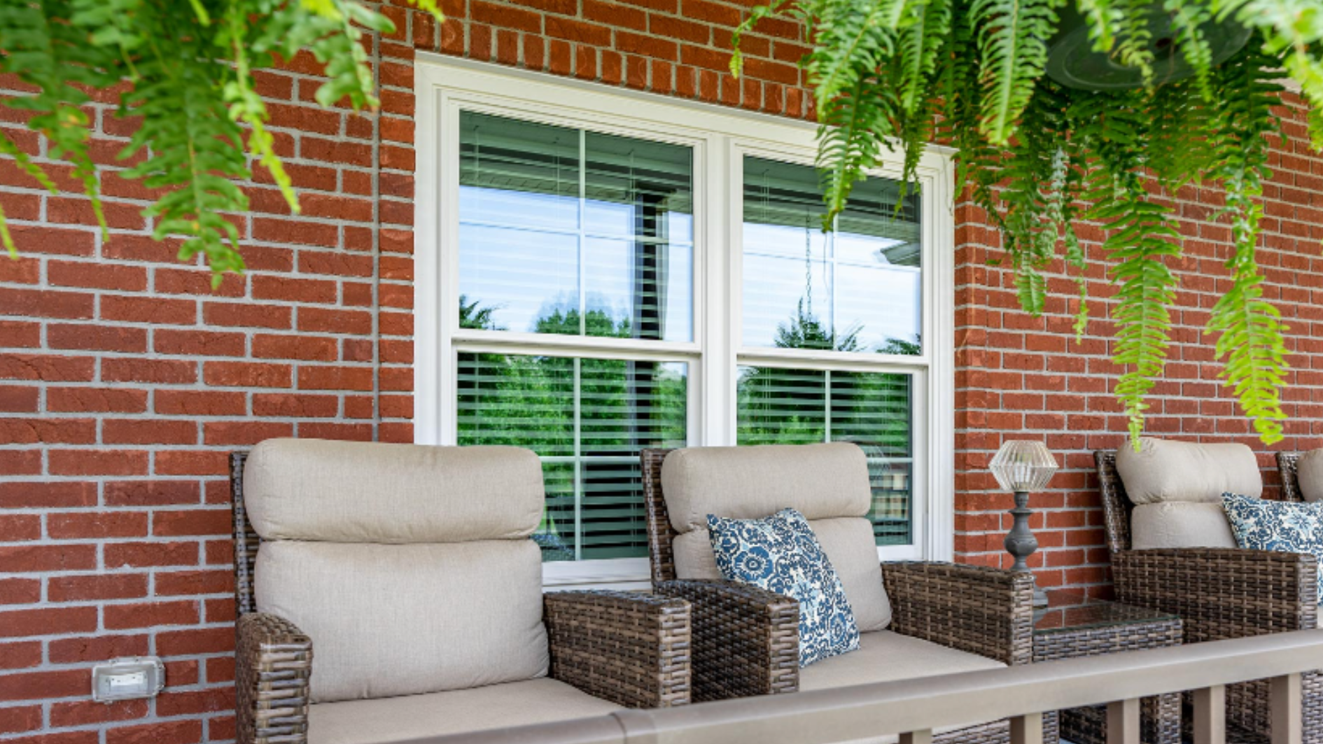 white ProVia double hung windows installed on a brick home exterior viewed from a covered porch with wicker furniture and hanging ferns