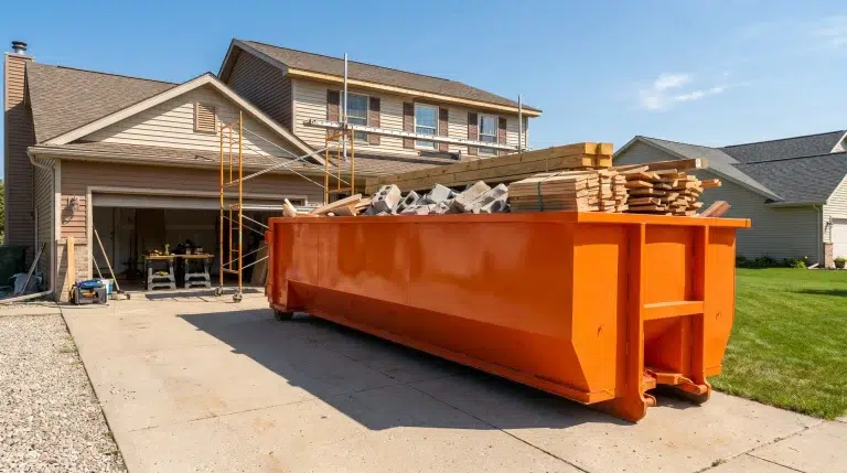 Large orange dumpster filled with construction materials outside house with scaffolding