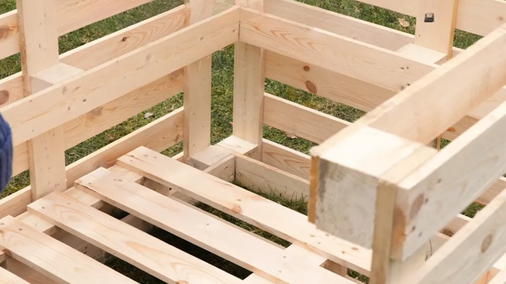 Wooden pallet structure with floor slats being placed inside the frame outdoors