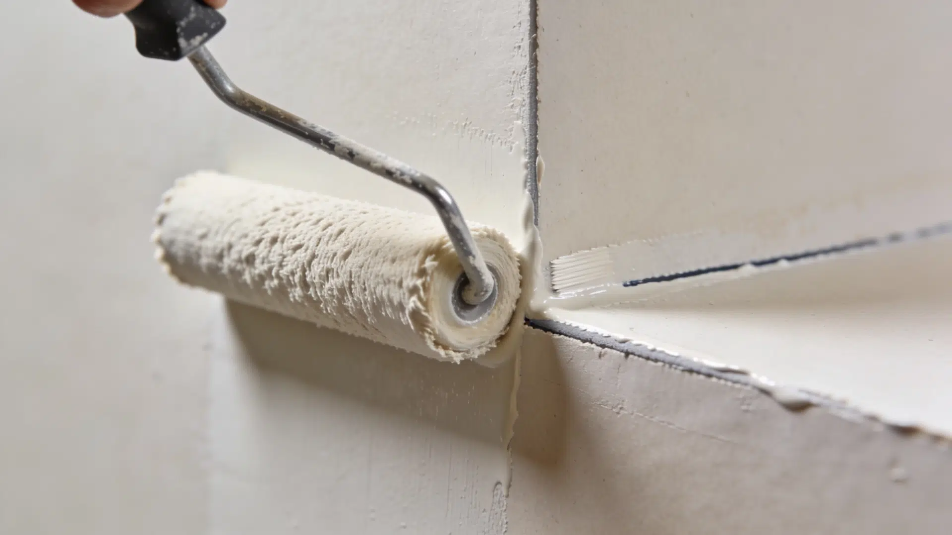 A roller applying a thin coat of paint to a wall, with a paintbrush used for edges.