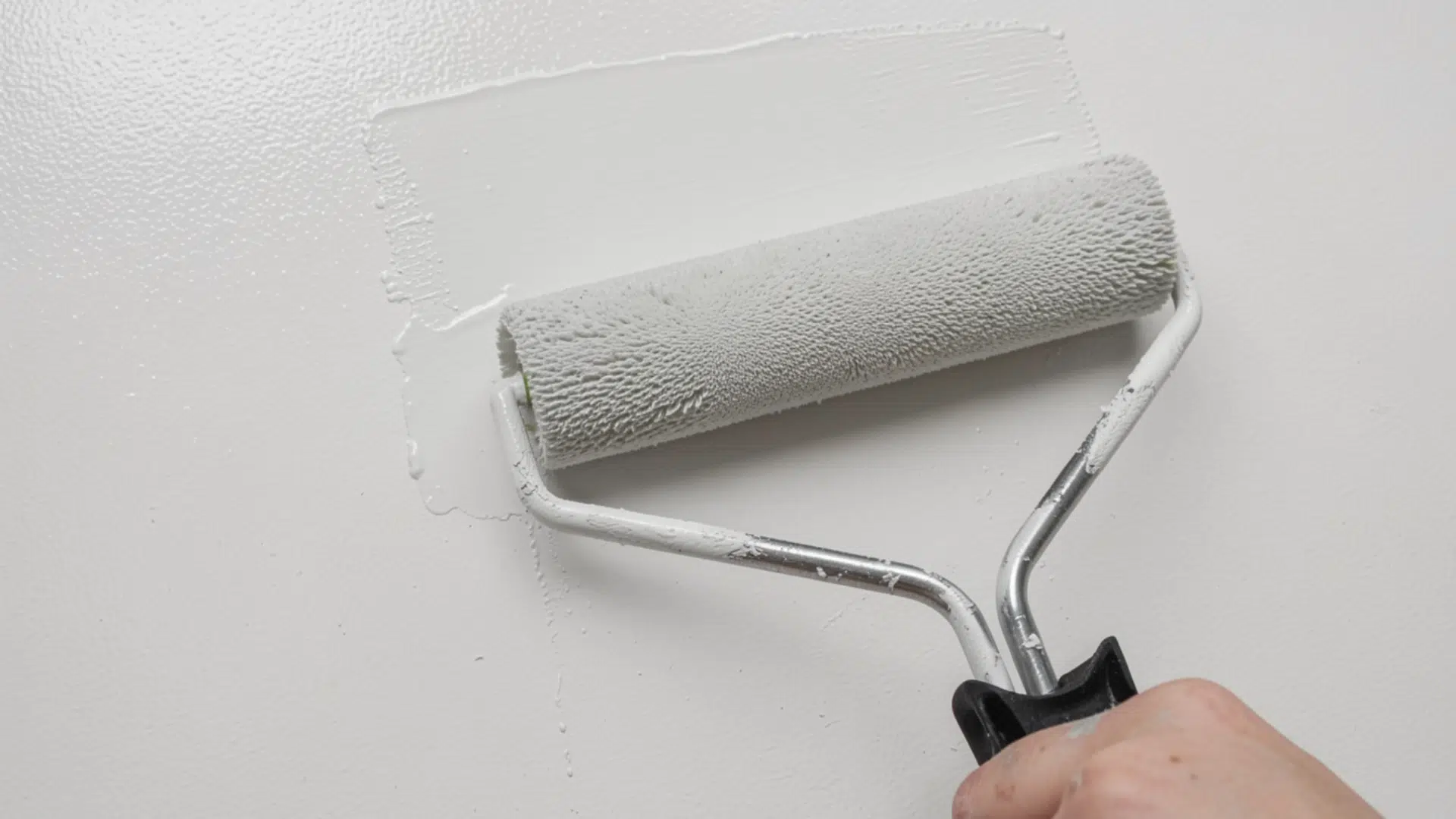 A roller applying a thin, even second coat of paint to a wall.
