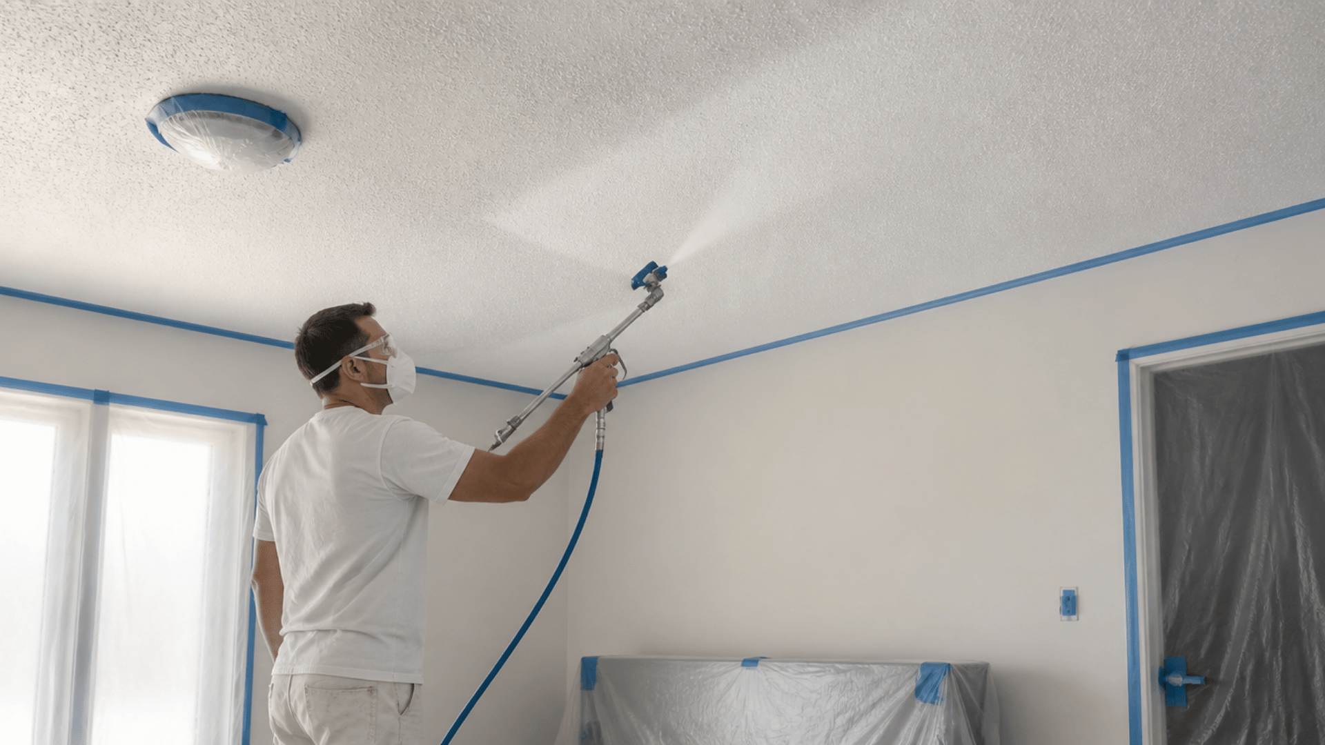 Airless sprayer applying light paint coverage to a popcorn ceiling.
