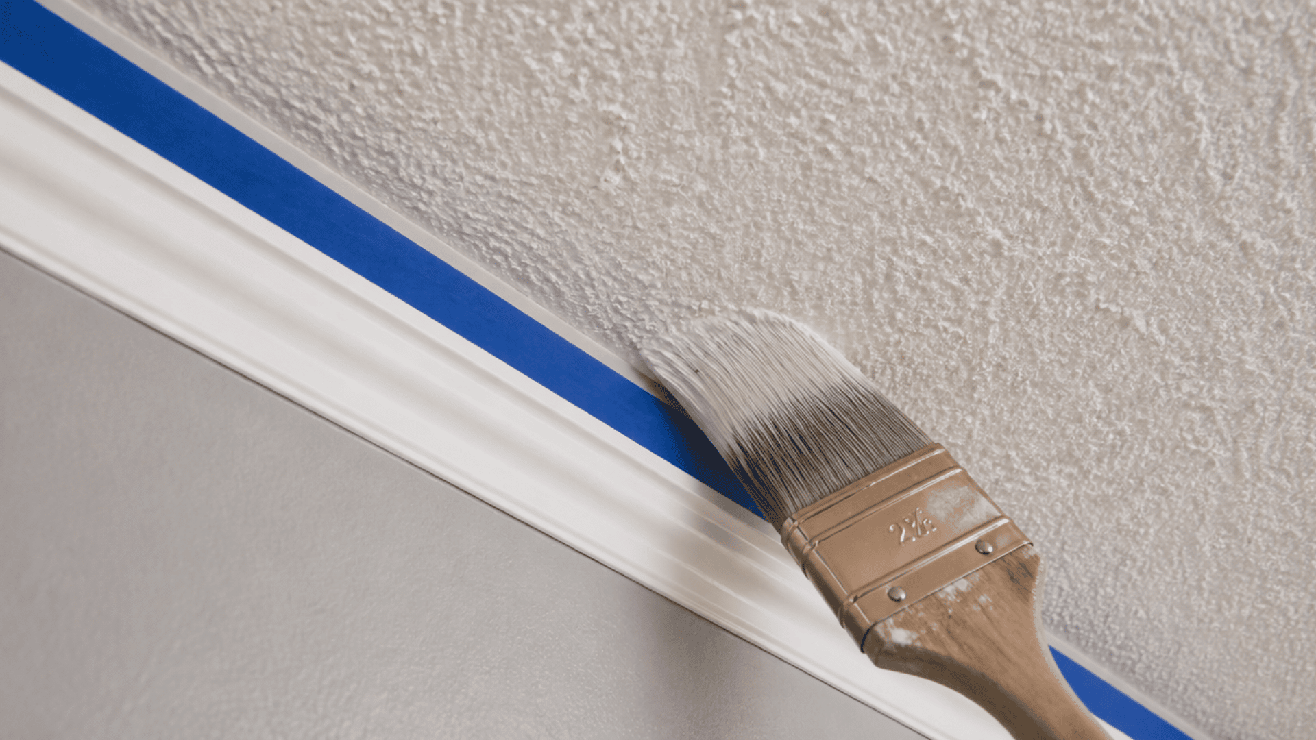 Angled brush painting the edge of a popcorn ceiling near taped wall trim.