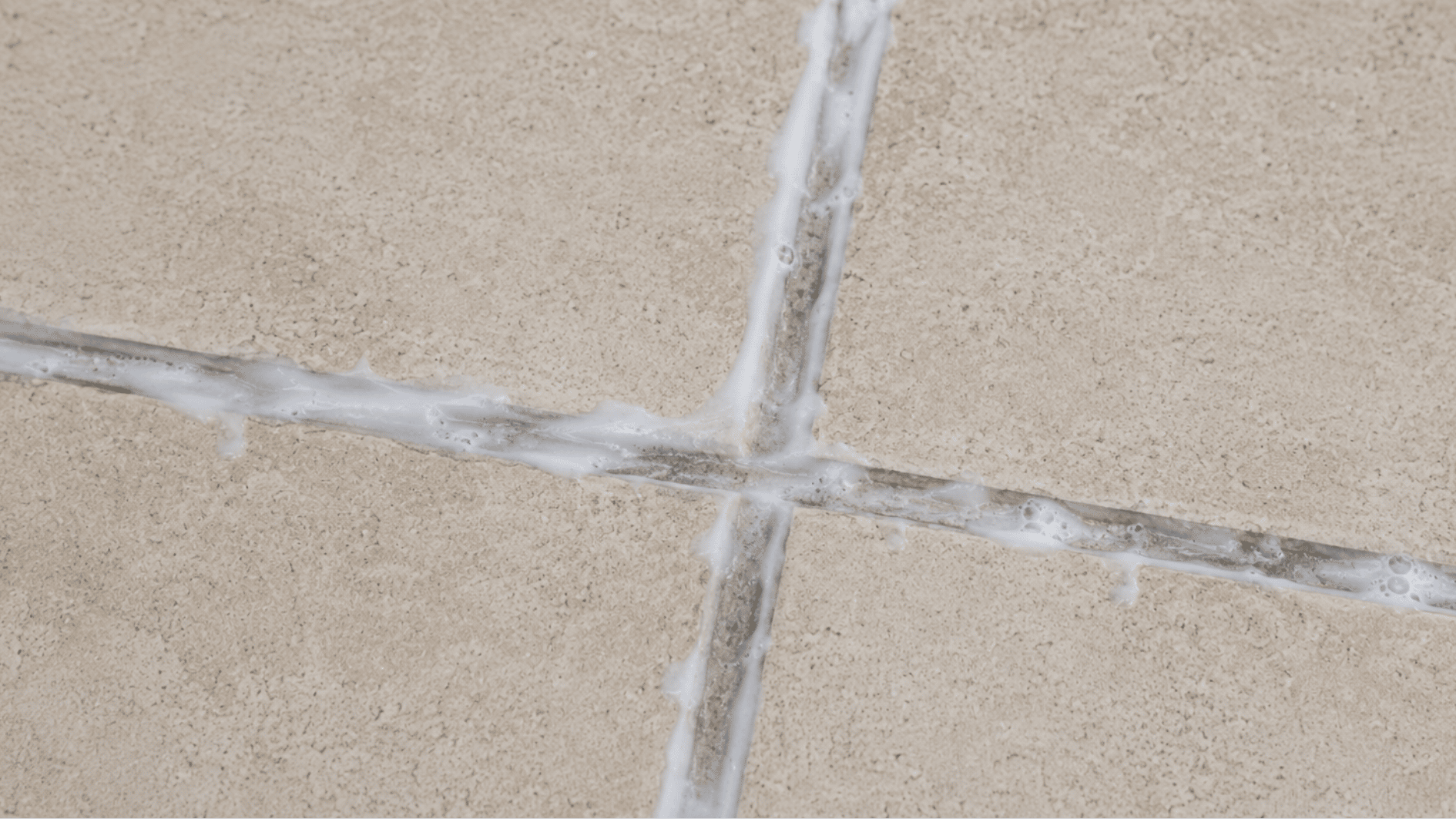 baking soda cleaning mixture sitting on dirty tile grout lines between beige floor tiles before scrubbing or rinsing