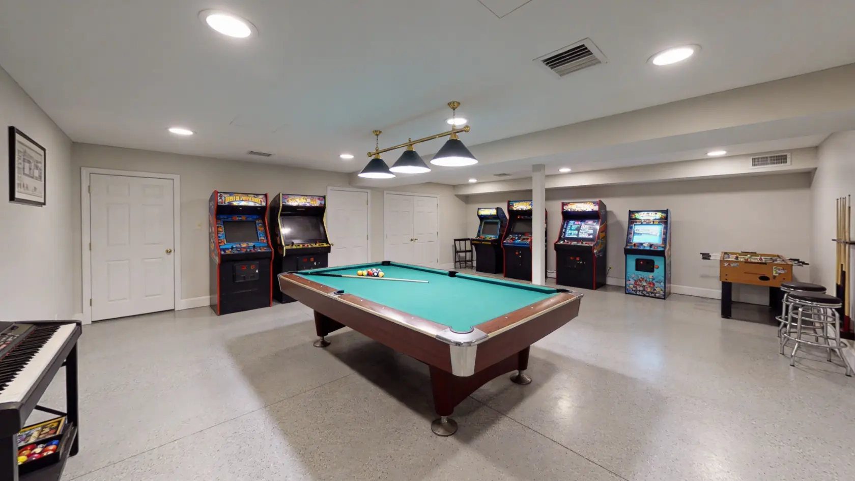 Basement game room with pool table in center, overhead light, and arcade machines along walls