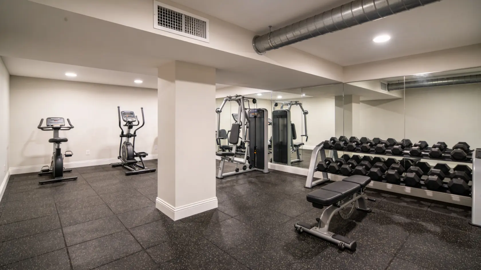 Basement gym with rubber flooring, exercise equipment, and multiple mirror on the wall