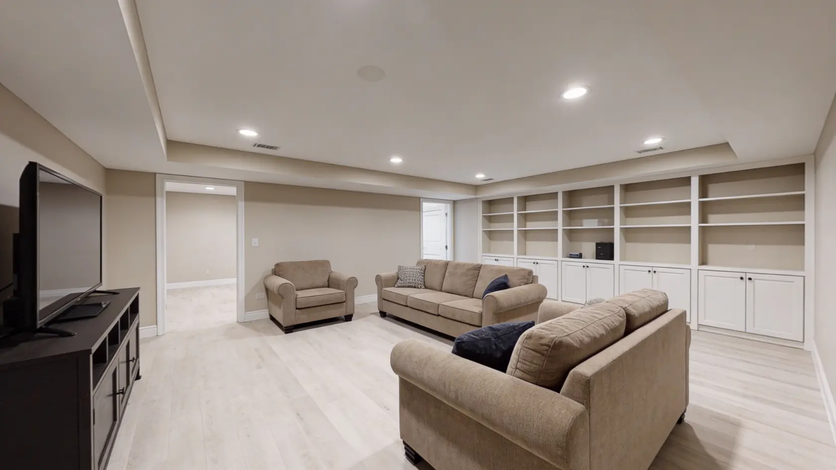 Basement living room with sofas, TV, storage units, and hard flooring in an open layout