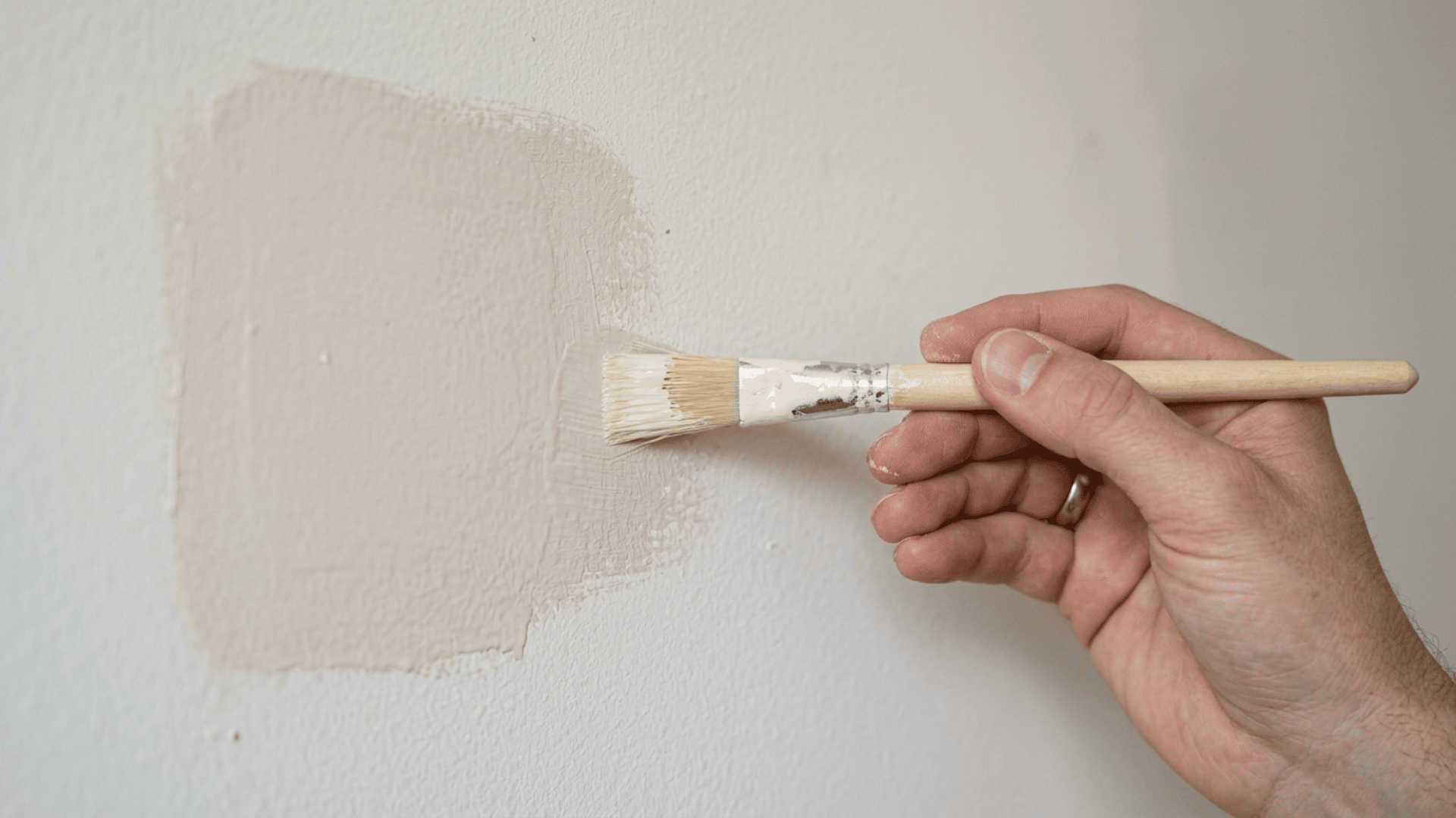 Hand painting a patched wall area with a brush, blending edges with the surrounding wall