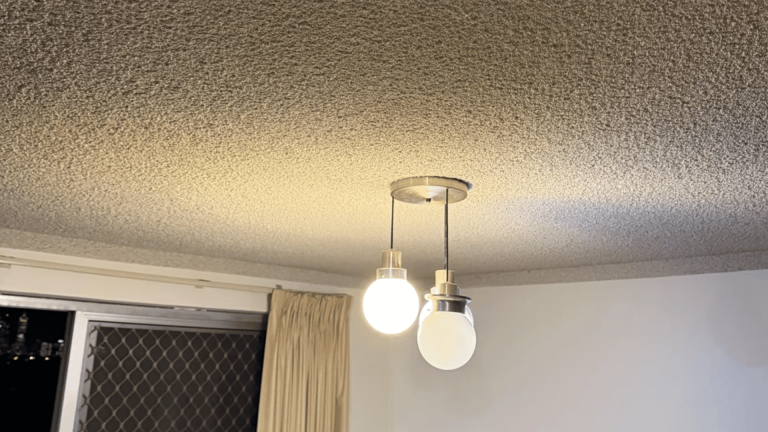 Ceiling with textured surface, two hanging light bulbs, sliding door with mesh screen, and beige curtain.