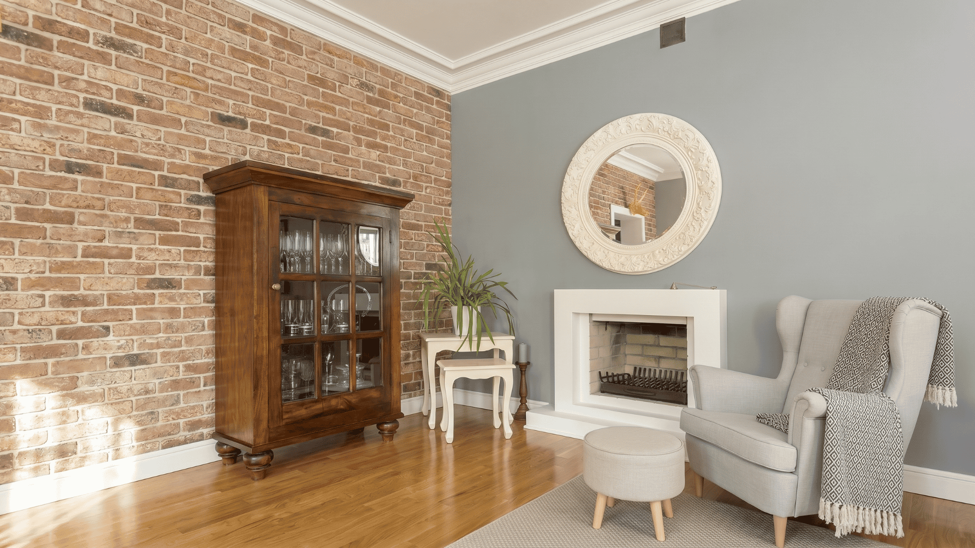 Living room with modern farmhouse style, featuring exposed brick, gray walls, white crown moulding, wooden cabinet, fireplace, and cozy seating
