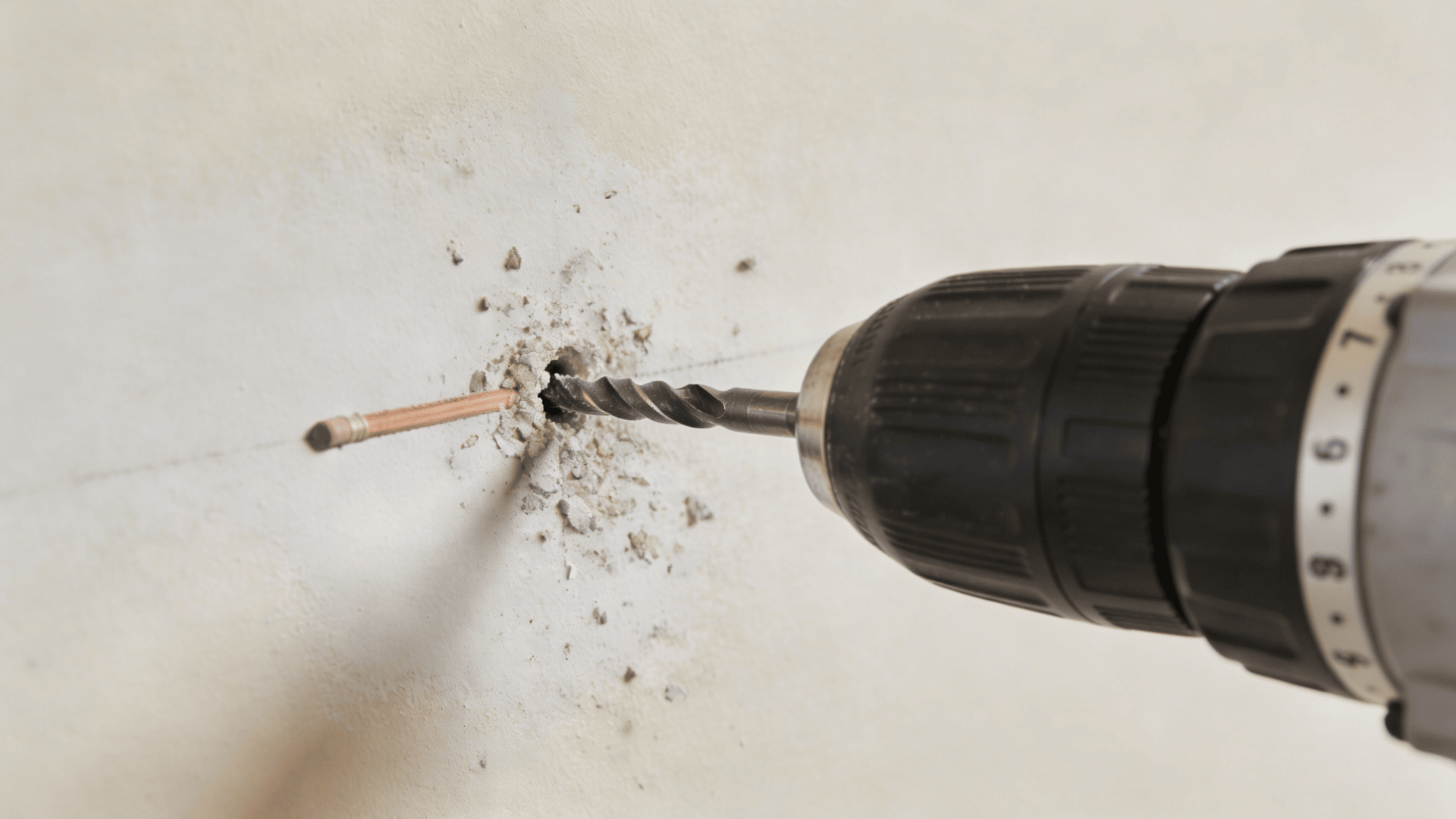 Drill bit boring a pilot hole into a wall with dust around the entry point.