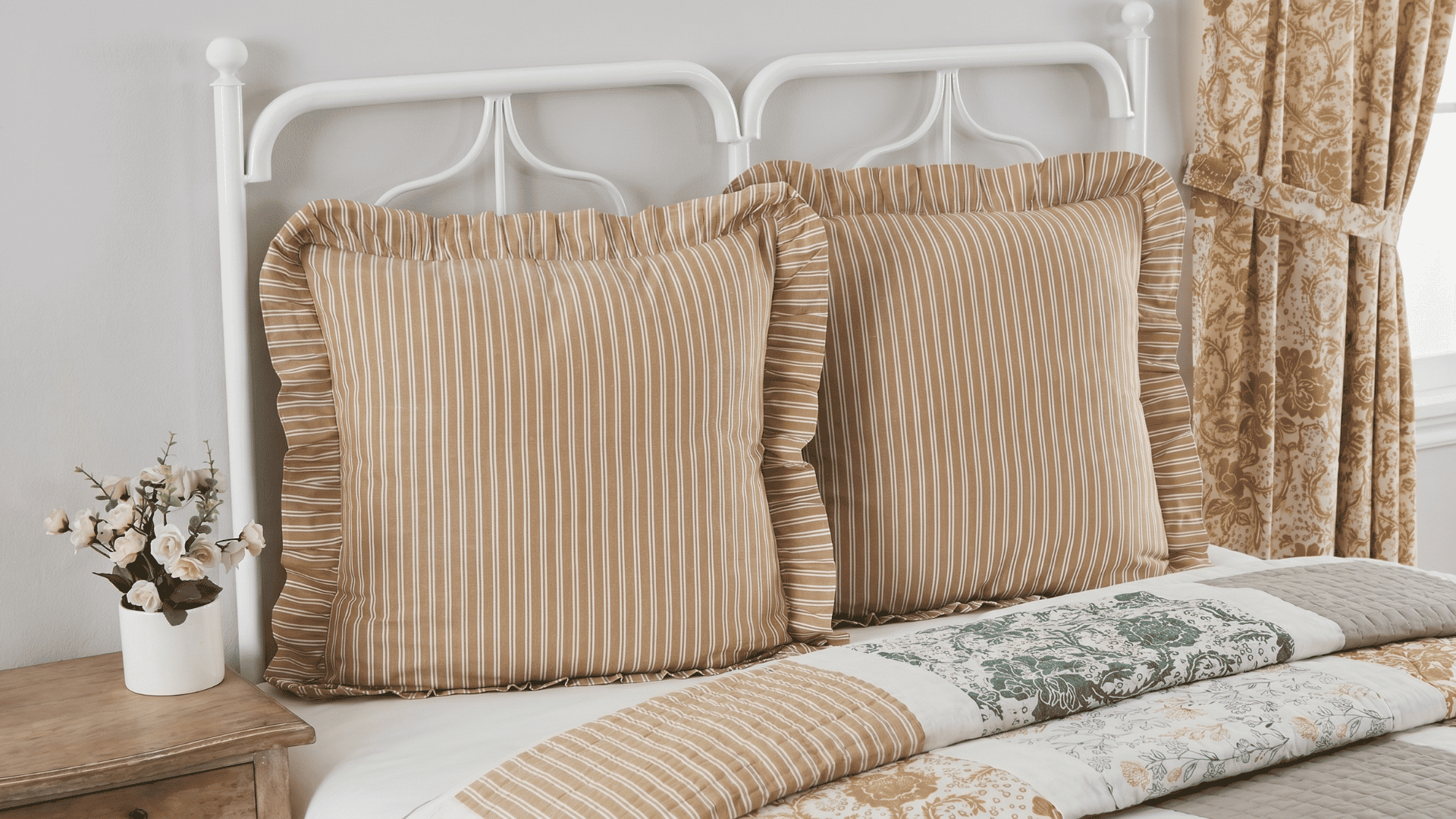 Striped Euro shams on a bed with a patchwork quilt and white metal headboard