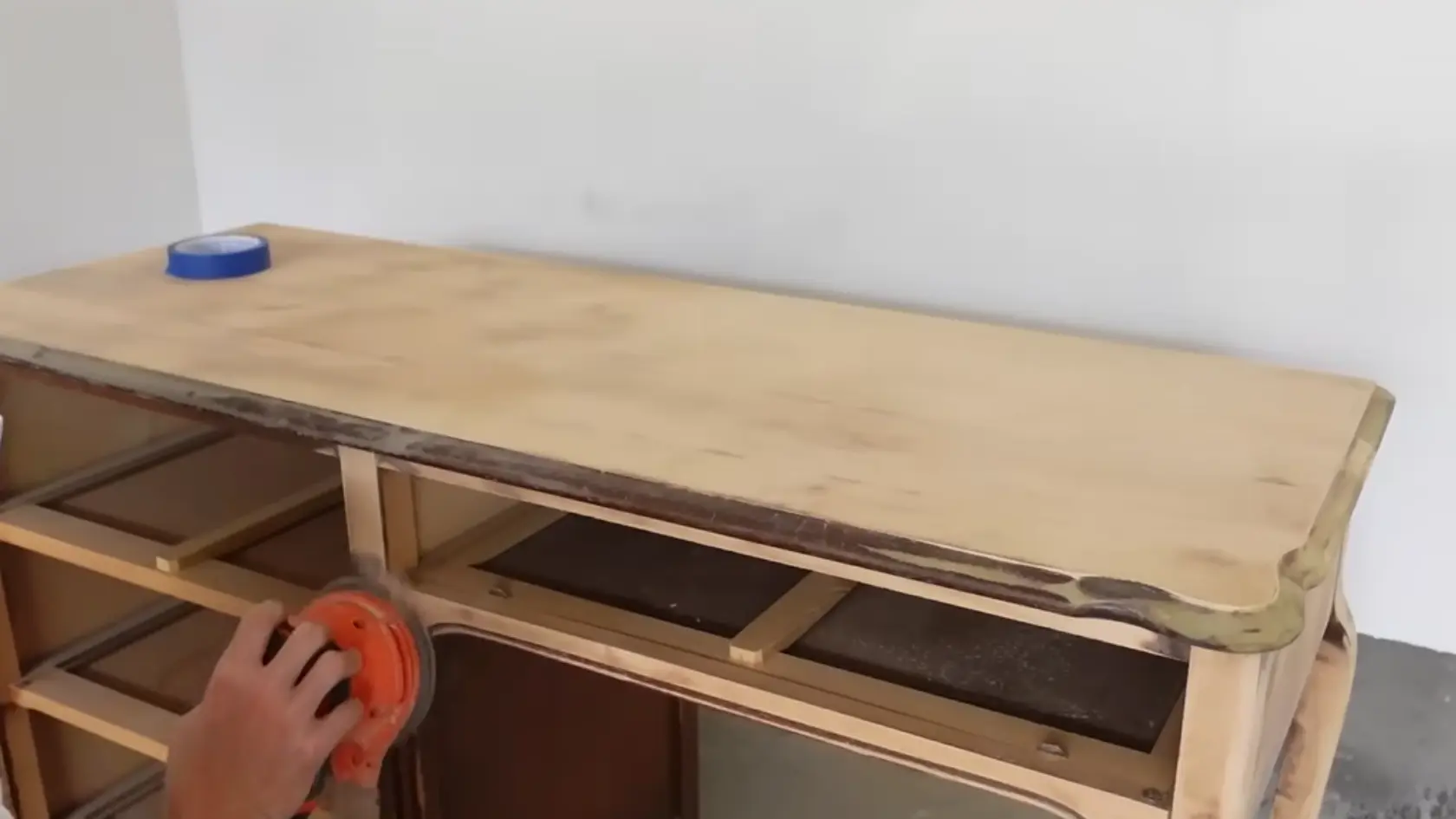 Hand using an electric sander to strip finish from a wooden desk surface during refinishing