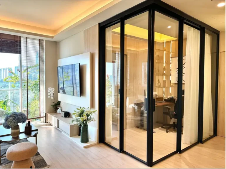 Modern living room with glass-enclosed office, wall-mounted TV, and floor-to-ceiling windows in bright setting