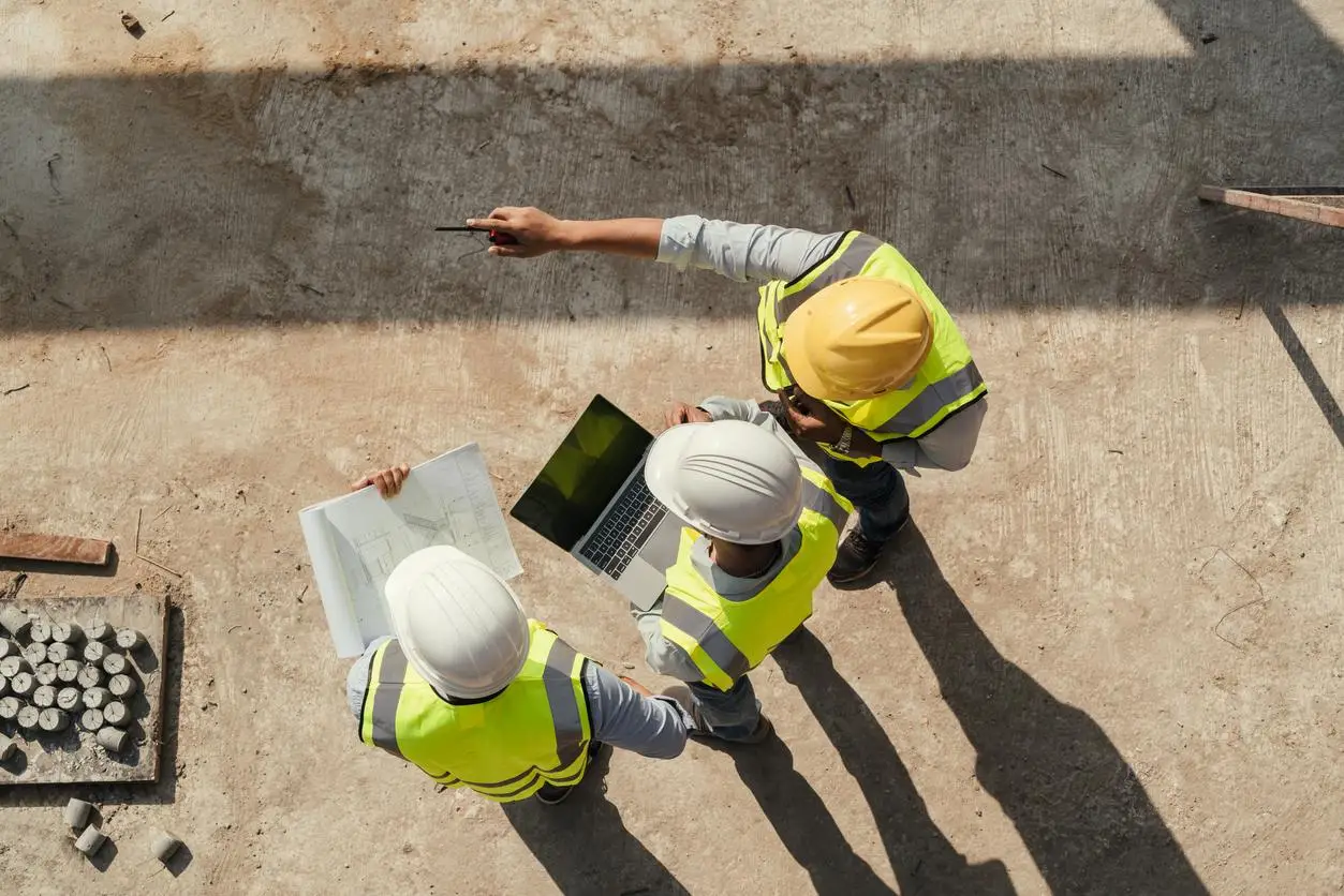 Construction workers in safety vests and helmets reviewing plans at a construction site