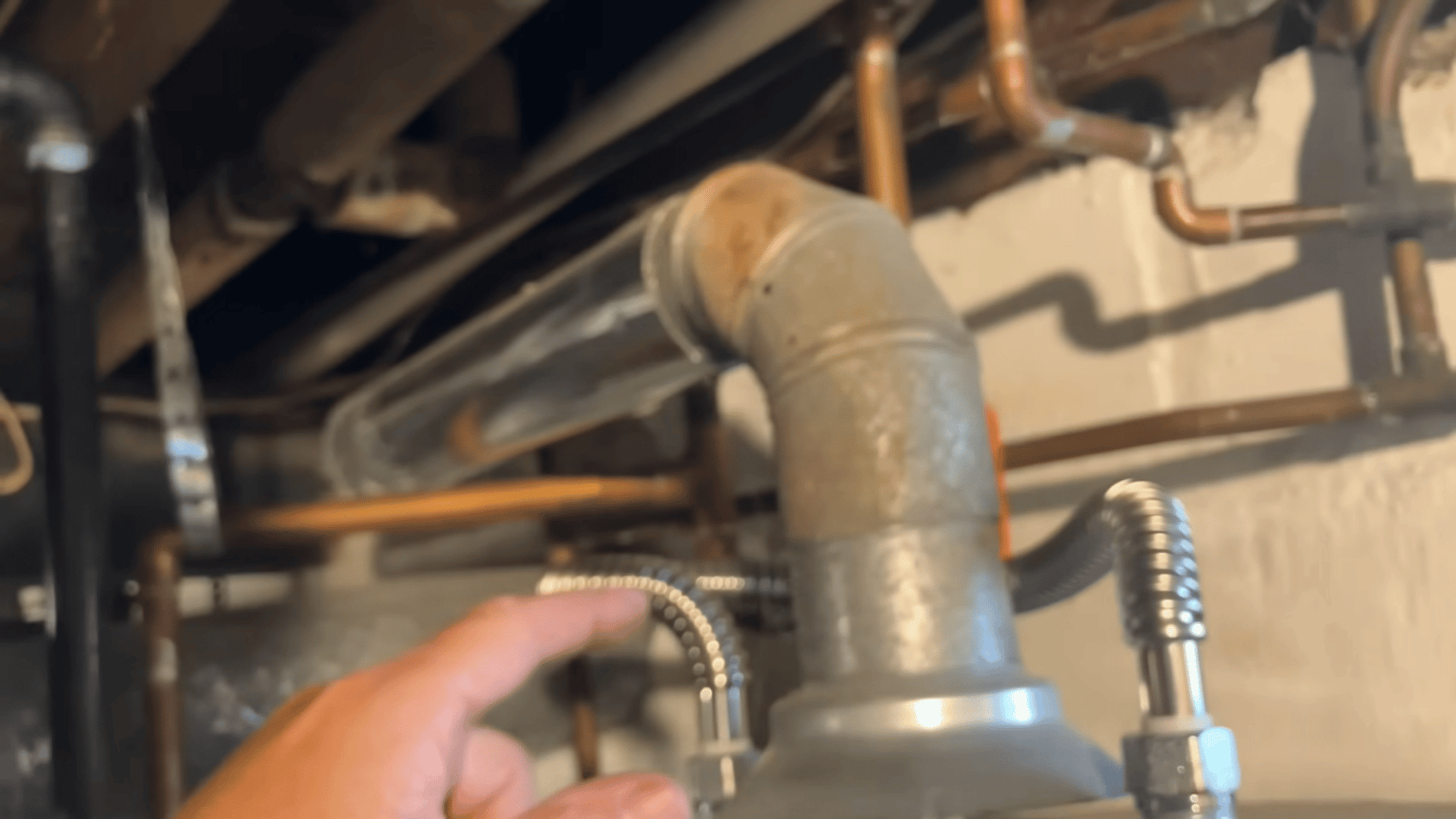 Hand holding a pipe connection on a boiler with visible metal fittings and surrounding pipes.
