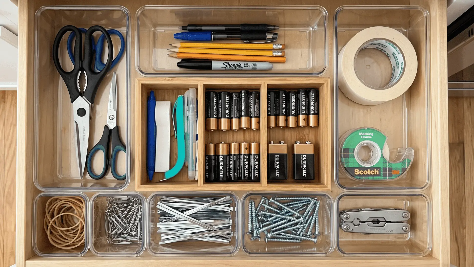 Kitchen junk drawer with trays separating batteries, scissors, tape, and pens