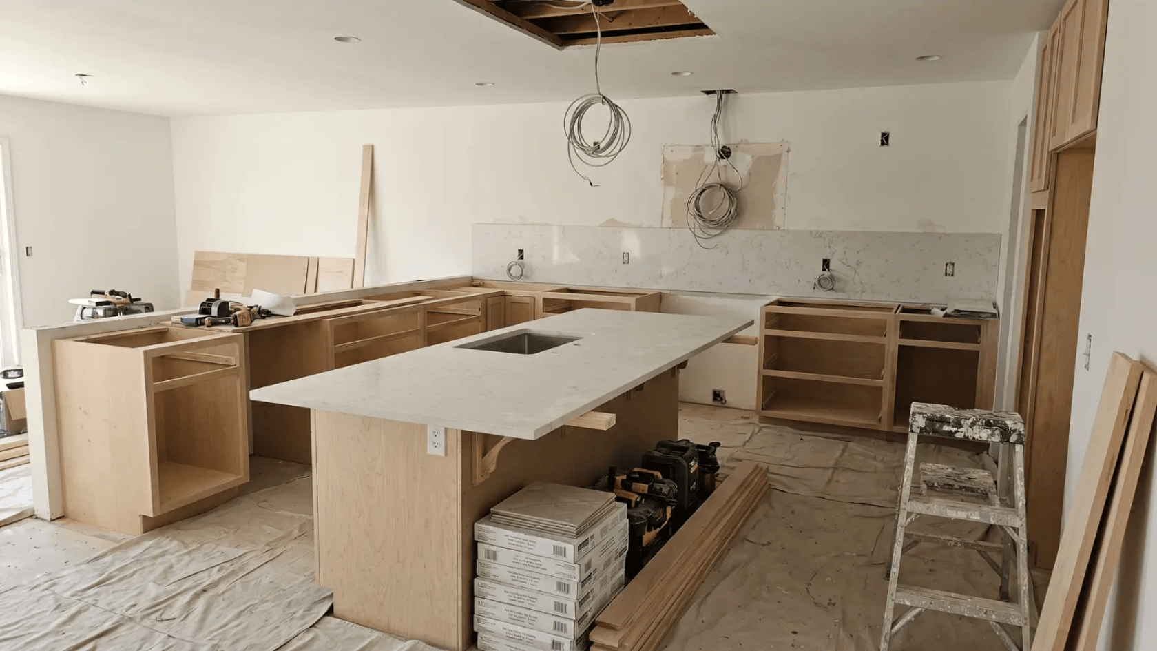 Kitchen under renovation with cabinets removed, countertops partially installed, and tools on the floor
