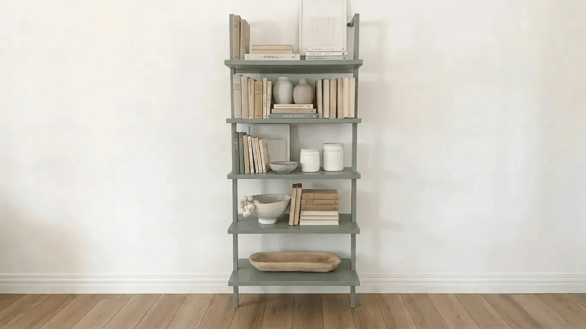 Minimalist bookshelf with neutral books, ceramics, and simple decor against a white wall.