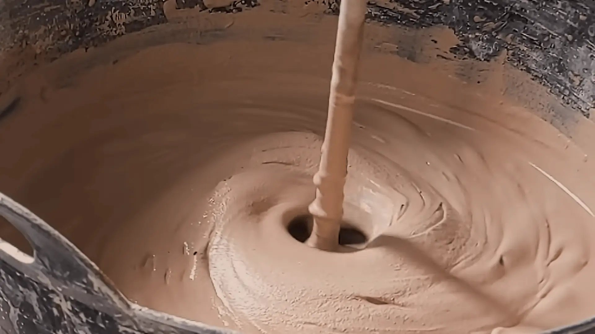 Mixing plaster in a tub to a smooth, yogurt-like consistency using a whisk, ready for application