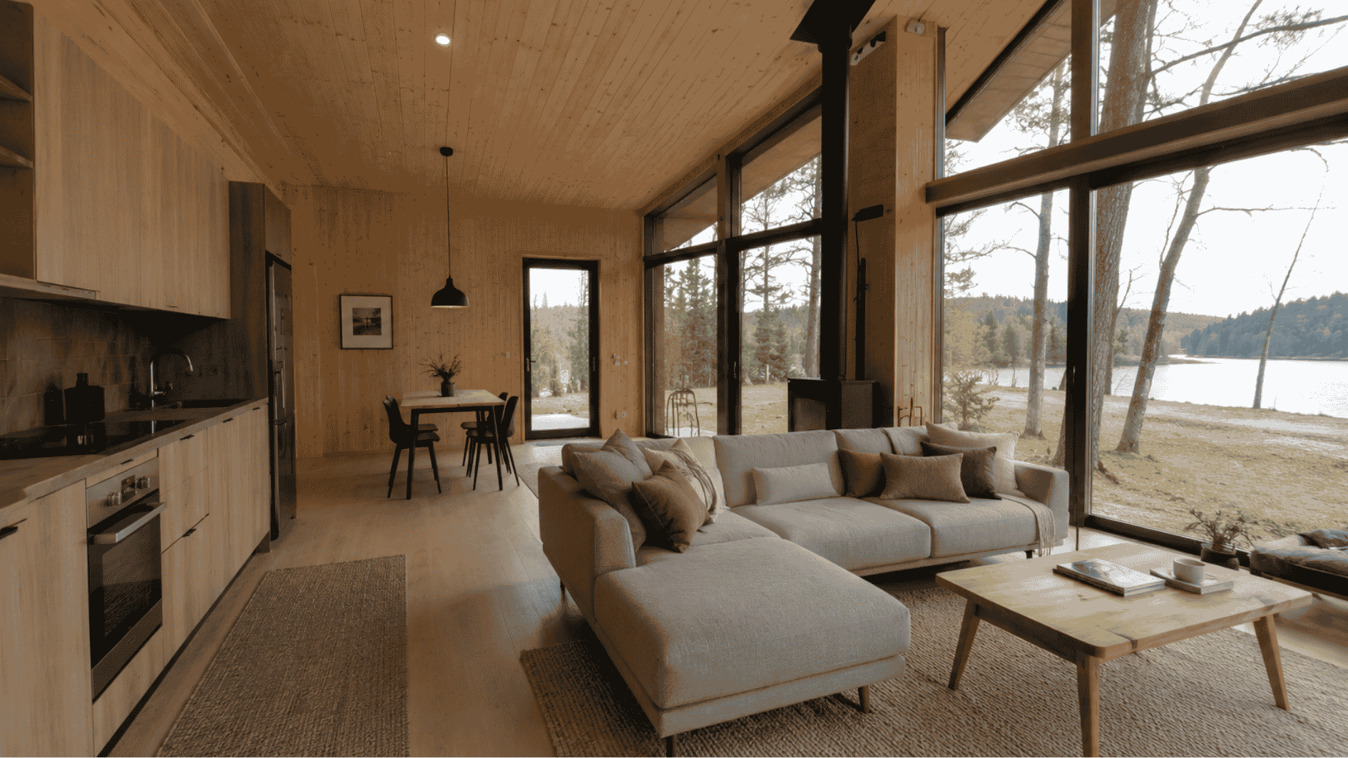 Modern prefab cabin interior with large windows, neutral furniture, wood walls, and lake views.