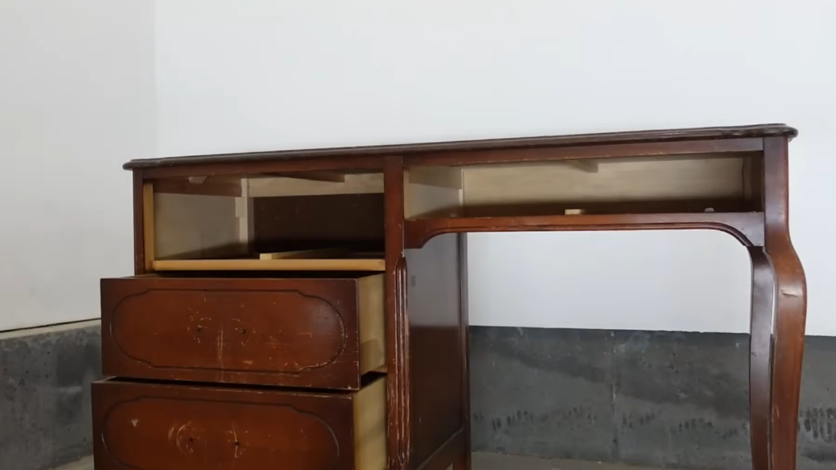 Old wooden desk with open drawers and worn finish against a wall