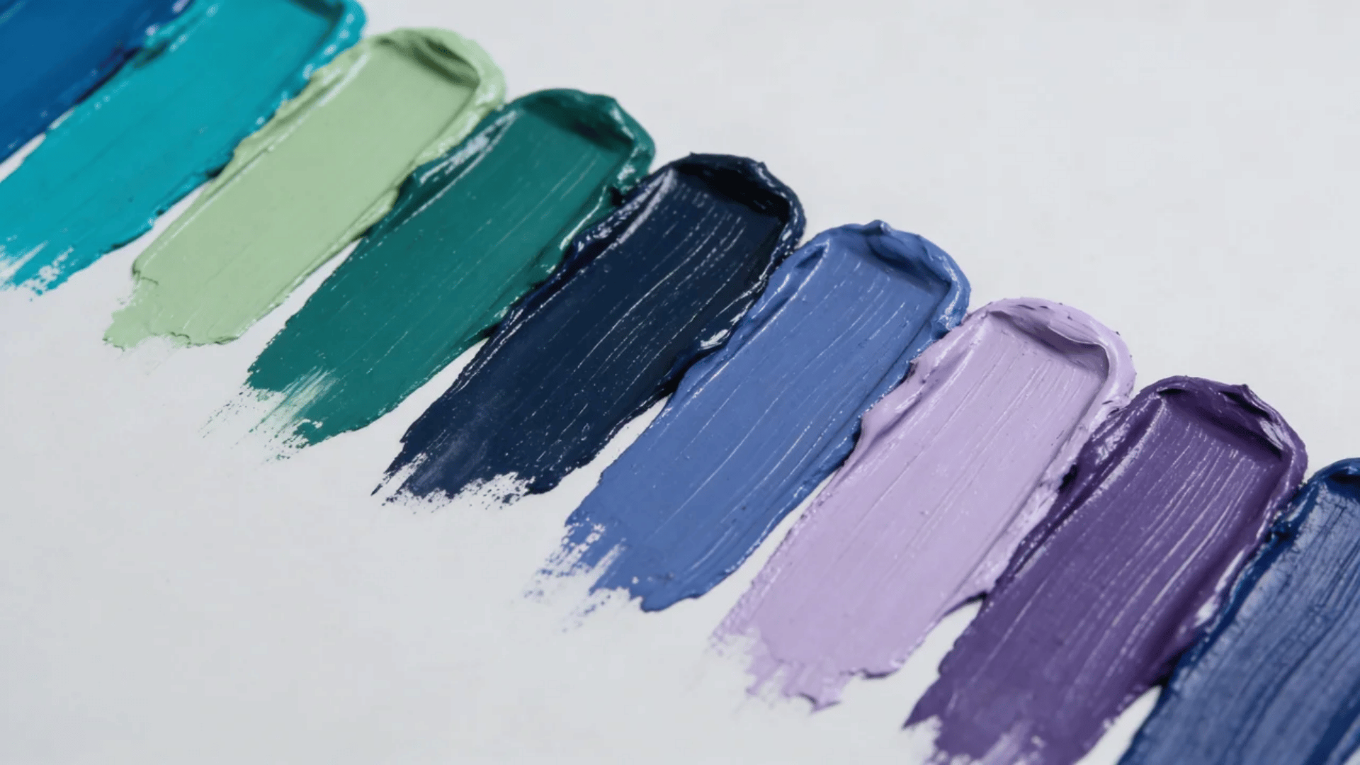 Paint swatches in blue, green, teal, sage, navy, lavender, and indigo arranged on a light grey surface.
