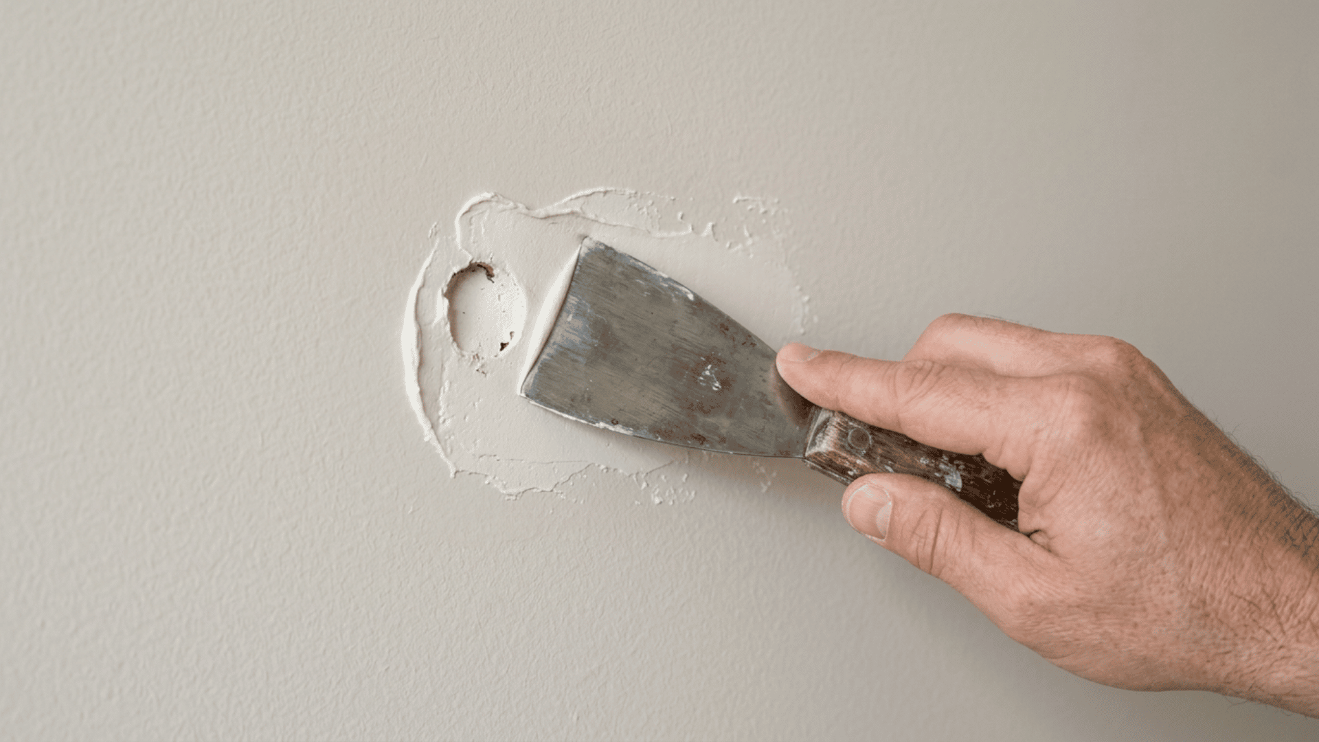 Hand applying spackle to a wall hole with a putty knife, smoothing the surface evenly