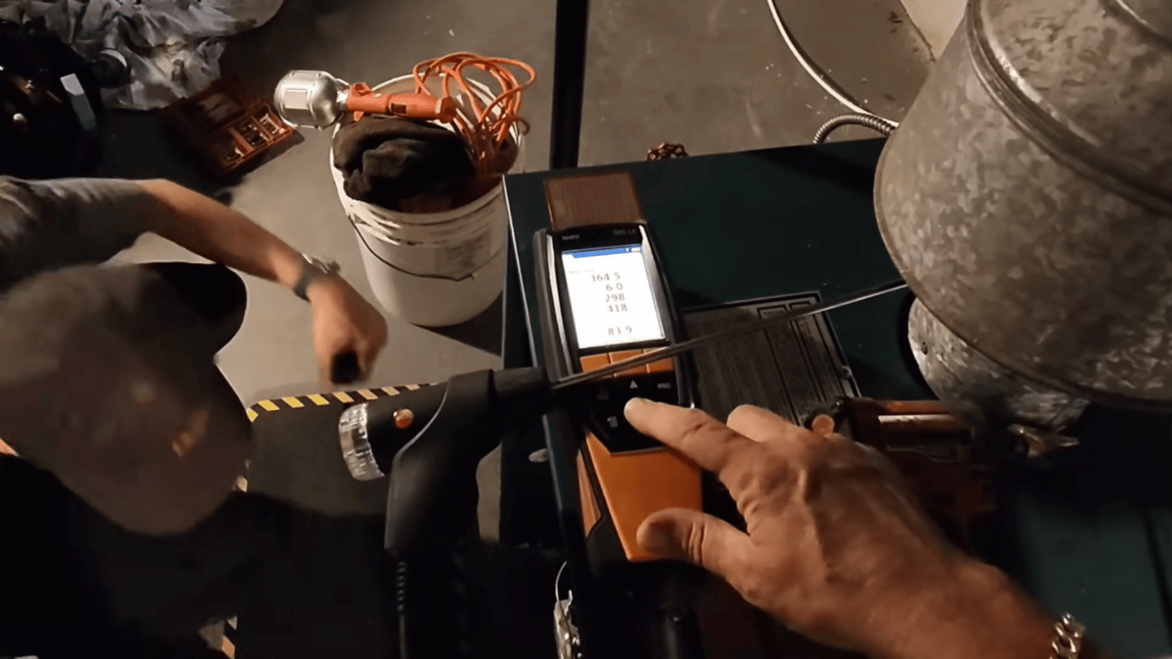 Technician holding a combustion analyzer and testing a boiler, with pipes and equipment visible around.