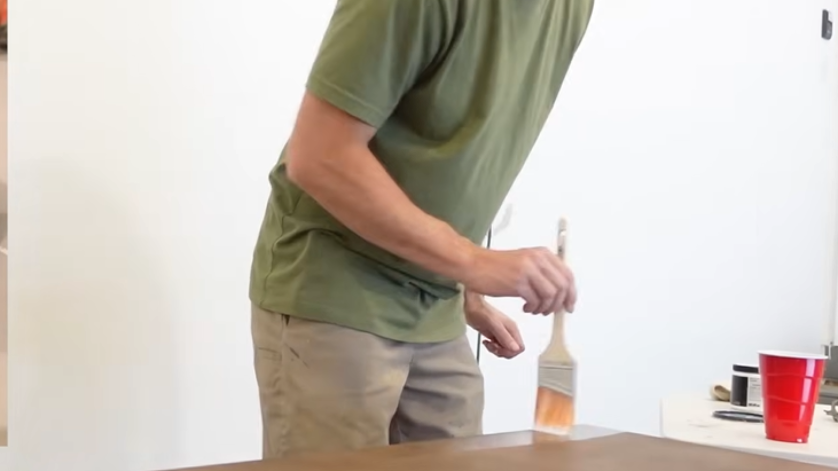 Person brushing finish onto a wooden tabletop during refinishing process