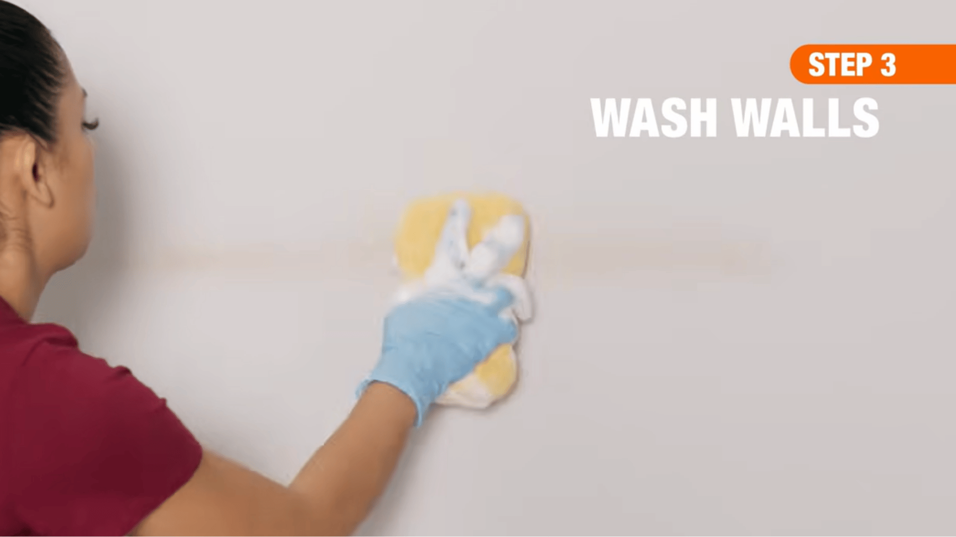 person washing a painted wall with a sponge and gentle cleaning solution to remove dirt without damaging paint.