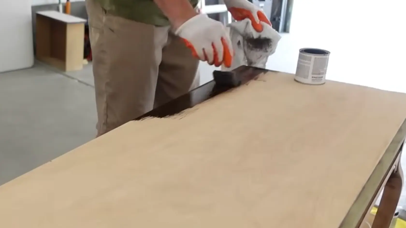 Person wearing gloves applying dark wood stain to a tabletop with a cloth and brush