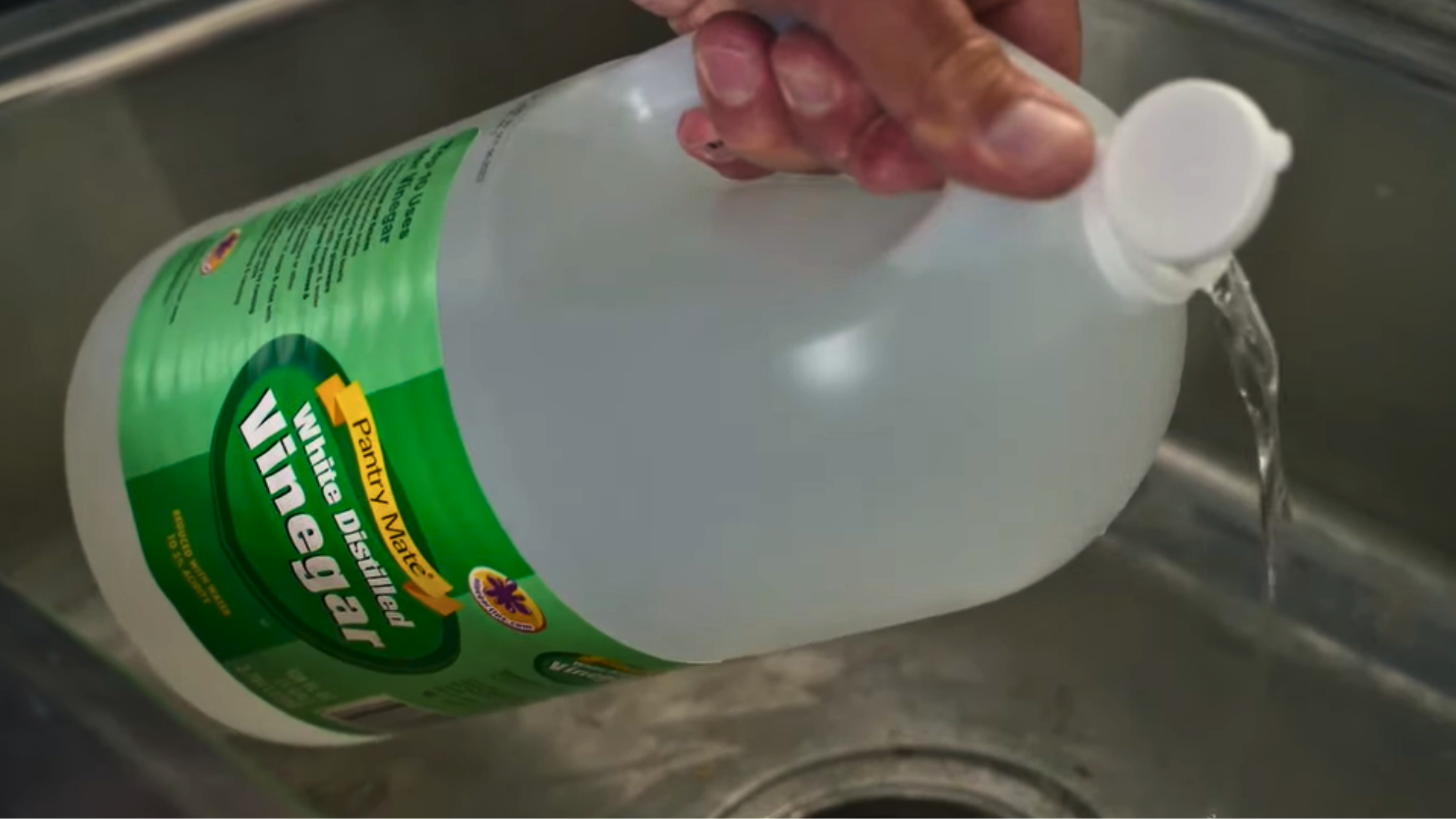 pouring white vinegar into a stainless steel sink to break down buildup