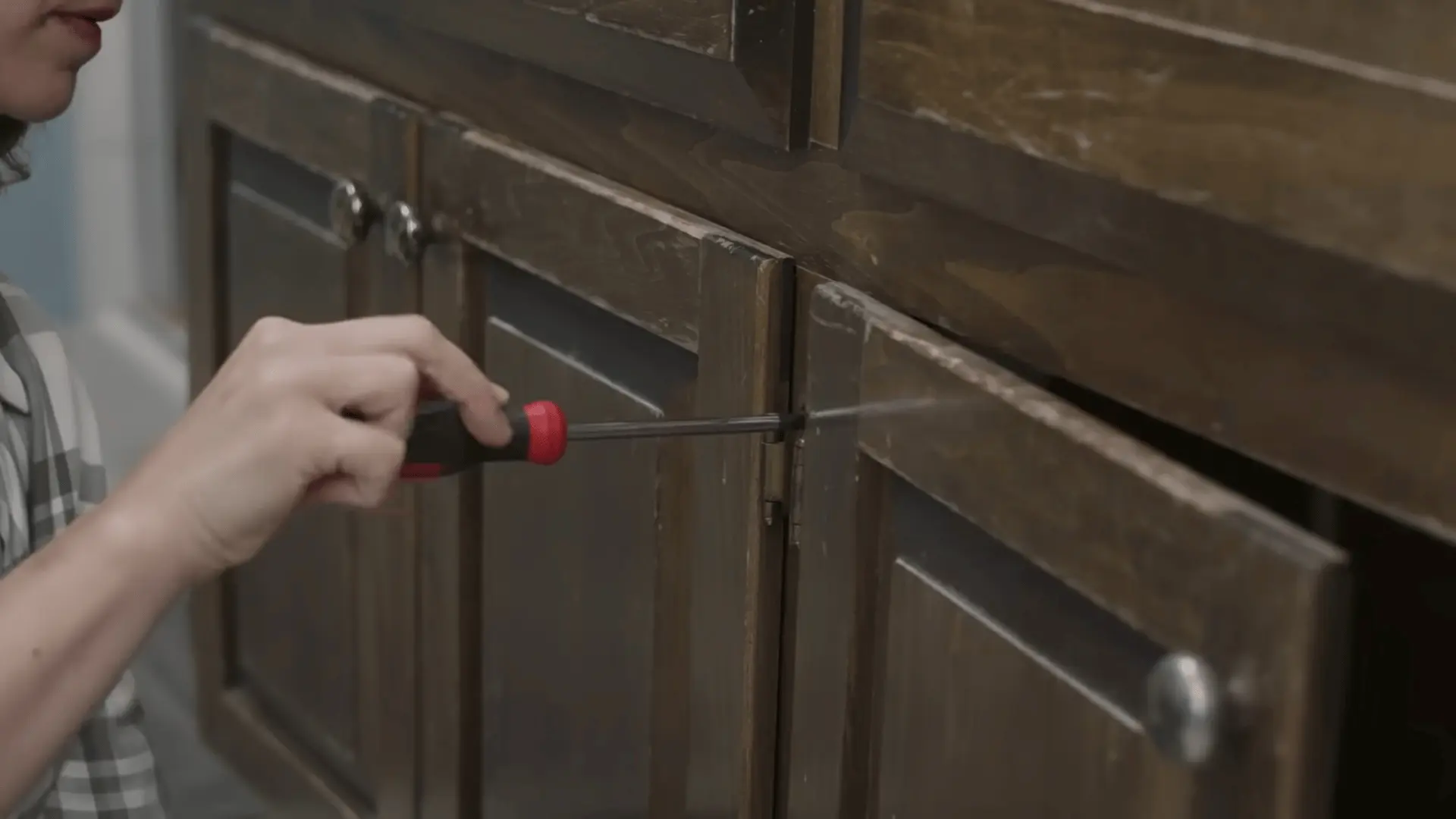 Removing hardware from the bathroom vanity doors using a screwdriver to prepare for painting