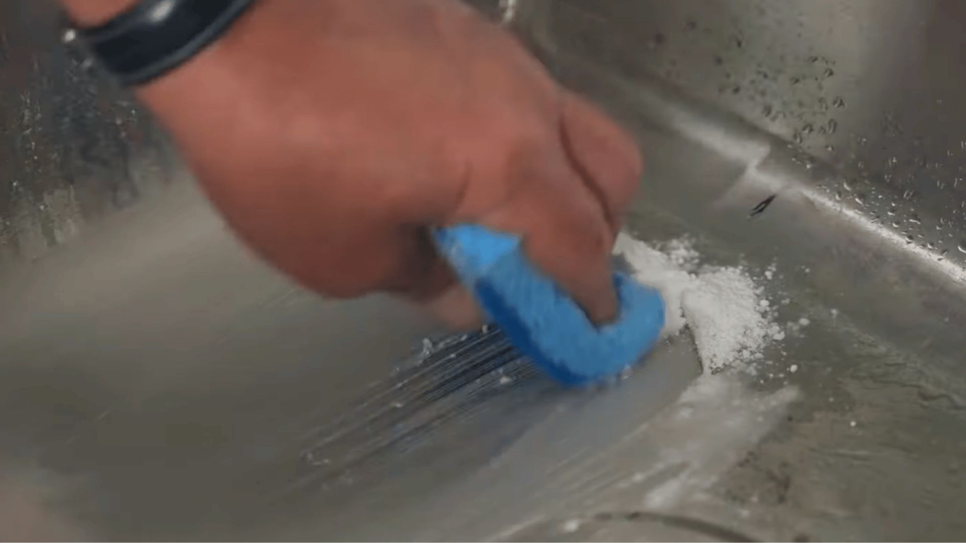 scrubbing a stainless steel sink with a sponge to remove stains and grime