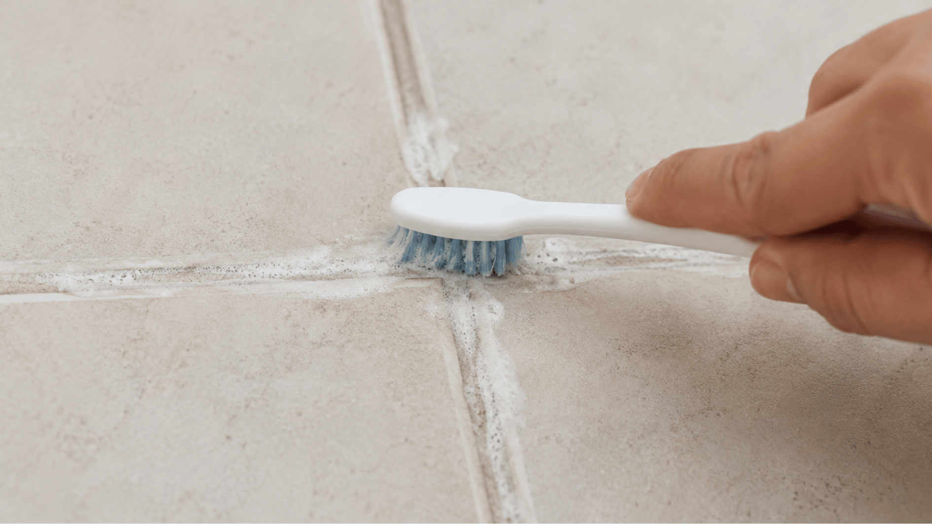 scrubbing grout lines with a toothbrush after applying baking soda cleaning paste